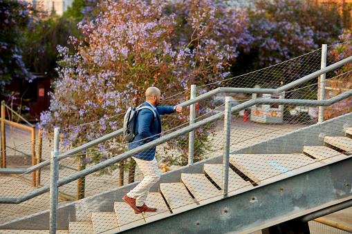 Full length side view of mid adult man in business attire and backpack hurrying up staircase to elevated walkway.