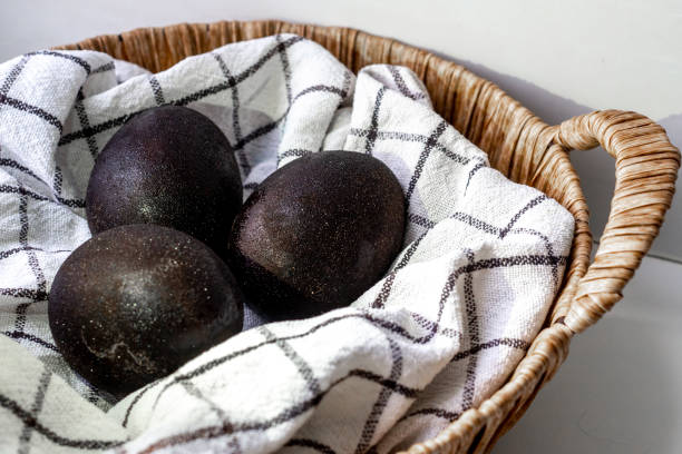 istock Black shiny easter eggs on a white towel in a brown basket on white background 1477452410