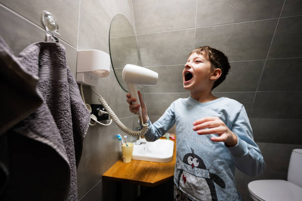istock Boy singing with a hair dryer at bathroom. 1477457407