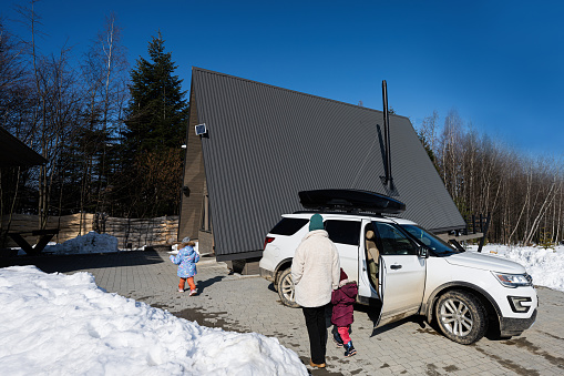 Mother and daughters against wooden triangle country tiny cabin house and suv car with roof rack in mountains.