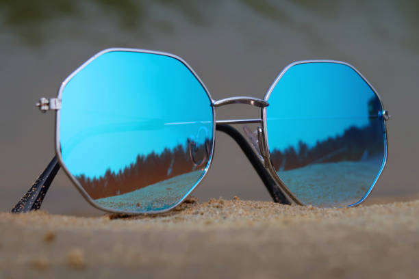 istock Full frame image of pair octagonal, metal framed, tinted, mirrored sunglasses on damp beach sand, sea background at low tide, focus on foreground 1477463019
