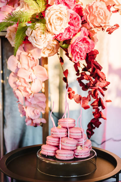 Cake macaroon with decor candles on table. Stylish luxury arch decorated with spring flowers tulips and greenery. Festive candy bar on photo zone for wedding. Birthday party celebration. Sunlights.