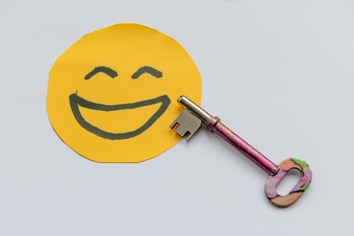 A key to happiness concept with a key and hand drawn happy face isolated in a white background.