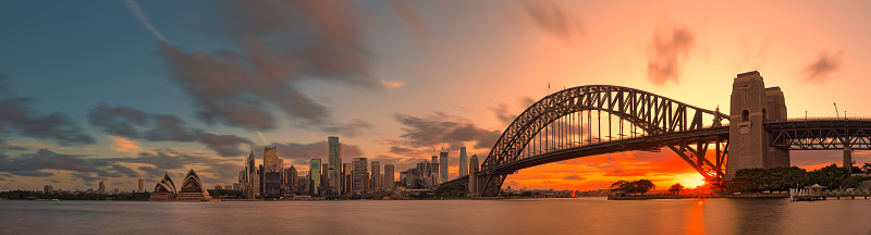 Sydney Harbour Bridge, Opera House and skyscrapers in the city are shrouded in pink afterglow under the reflection of the setting sun.