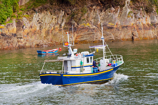 Rear view of fishing boat going into Viavélez harbor,  sea water,stone cliff in the  background. Asturias, Spain.