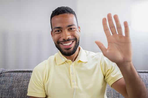 Portrait of smiling businessman waving hand during video conference call.