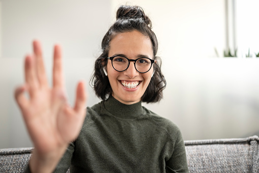 Portrait of smiling businesswoman waving hand during video conference call.