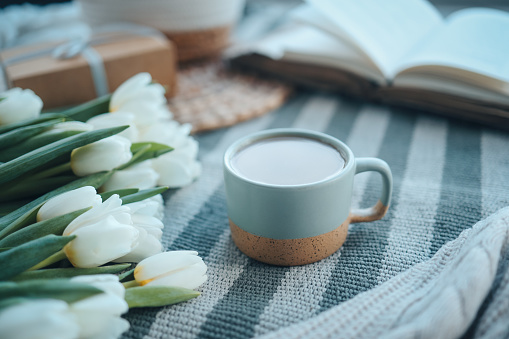 A cup of cappuccino, a bouquet of tulips, an open book and a gift, good morning aesthetics.