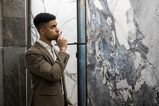 Nicely dressed black salesman seen standing in front of some exclusive ceramic tiles in a showroom before opening.