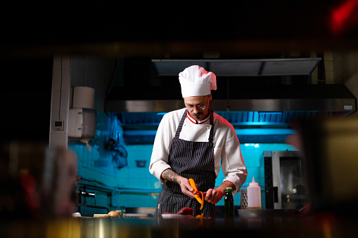 Professional chef peeling fresh carrot while preparing a meal in commercial kitchen.