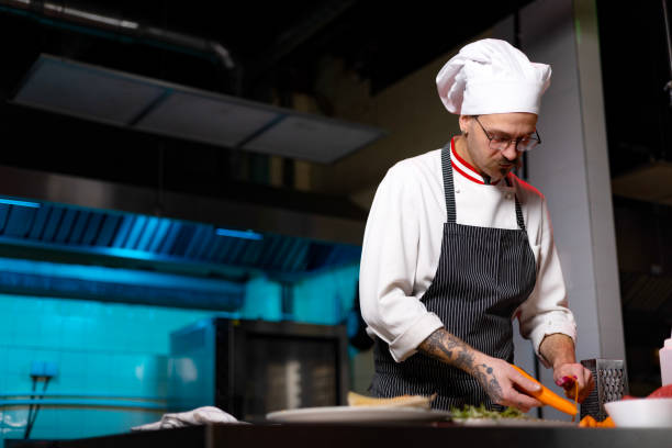 istock Young male chef peeling fresh carrot in the kitchen. 1477475005