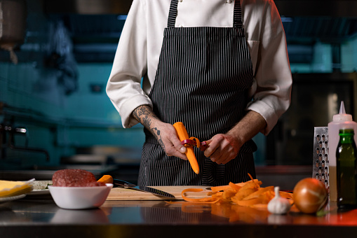 Unrecognizable male chef peeling carrot while preparing a meal in the kitchen.