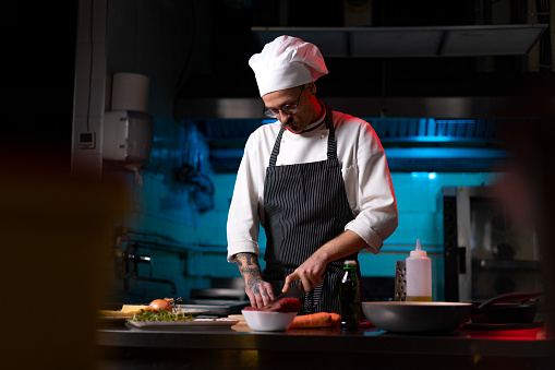 Young male chef cutting vegetables for a meal in commercial kitchen.