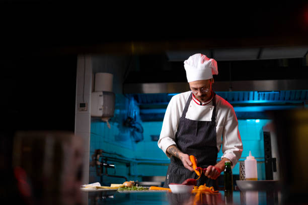 istock Young male chef peeling carrot in the kitchen. 1477475694