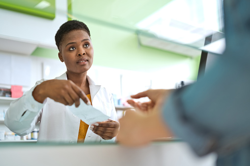 Female pharmacists talking with customer, holding prescription in hand. They are standing in pharmacy.