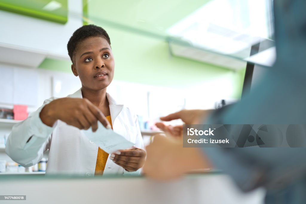 Female pharmacist talking with customer Female pharmacists talking with customer, holding prescription in hand. They are standing in pharmacy. Pharmacist Stock Photo