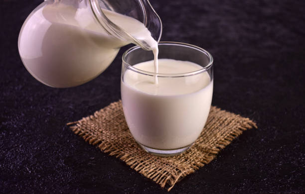 istock Milk is poured into a glass on a black background . 1477480989