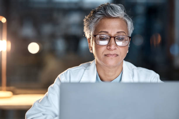 Woman, doctor and laptop in office at night at workplace, hospital or desk for medical career vision. Healthcare expert, dark clinic or focus for reading at computer, email or cancer research article mujer, médico y computadora portátil en la oficina por la noche en el lugar de trabajo, hospital o escritorio para la visión de la carrera médica. experto en atención médica, clínica oscura o enfoque para leer en computadora, correo electrónico o a