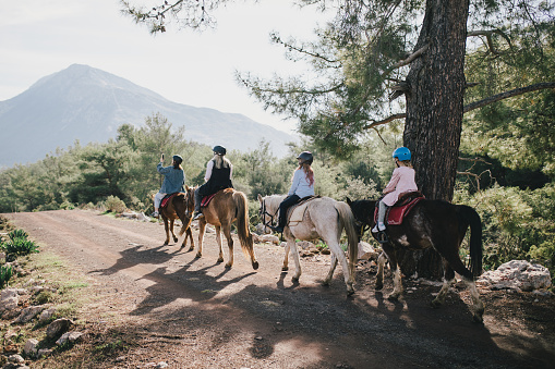 A young woman takes photos of a group of people on her smartphone  riding a horse through picturesque landscapes.