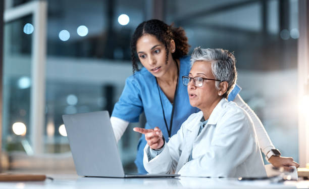 Doctors, nurse or laptop in night healthcare, planning research or surgery teamwork in wellness hospital. Talking, thinking or medical women on technology for collaboration help or life insurance app stock photo