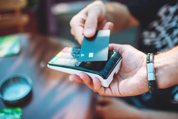 Adult man paying with credit card at cafe, close-up of hands with credit card and credit card reader stock photo