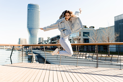 Portrait of a beautiful young woman enjoying music, jumping and having fun by the river