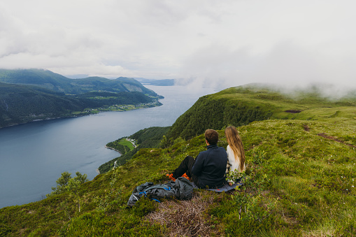 Woman and man backpackers relaxing on top of the mountain looking at dramatic summer landscape of Norway's nature in Scandinavia