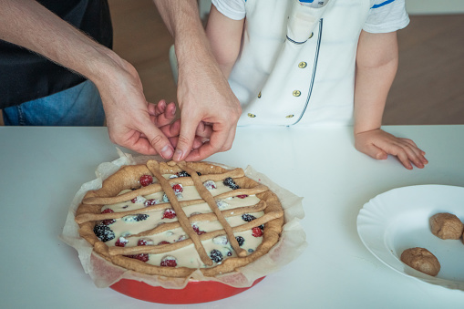 A man and a child are cutting a pie with berries on top.