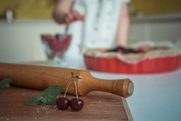 A cherry with leaves sitts near a rolling pin on the kitchen desk, close-up