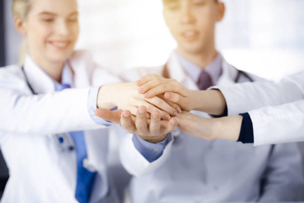 istock Group of doctors joining hands as a circle and ready to help patients while sitting at the desk in modern hospital office. Successful teamwork in medicine, Coronavirus countering concept 1477488371