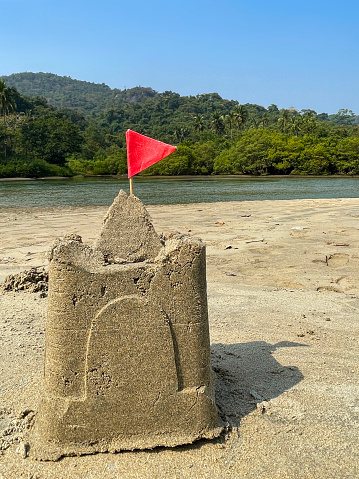 Stock photo showing sandy beach with a sandcastle made with a bucket with a mold shape, in the distant background the sea and a large group of trees can be seen