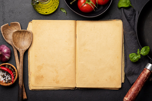 Top-down view of a kitchen table with ingredients, utensils, and an open cookbook with empty pages, perfect for creating a mockup for recipes or menus