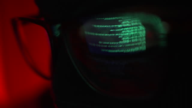 Hacker in a mask and glasses close-up tries to hack into the server, the reflection of the code in the lens of the glasses