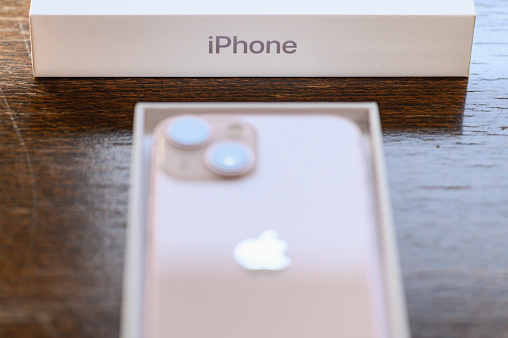 Studio shot of an iPhone 13 mini pink, from above on a wooden table. Focus on an Apple name
