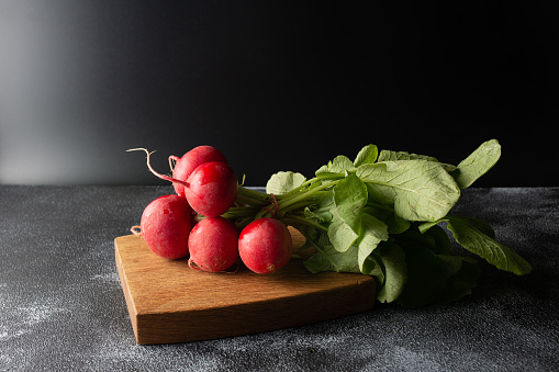 fresh radishes bunch on a wooden board on a dark background. Copy space.