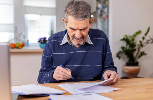 A senior adult man sitting at a table stacked with papers stock photo