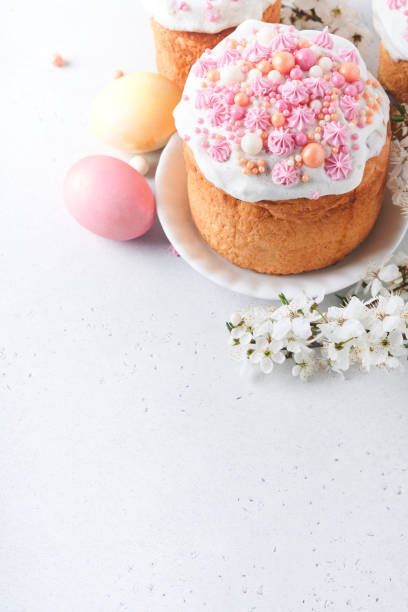 istock Traditional Easter sweet bread or cakes with white icing and sugar decor, colored eggs and cherry blossom tree branch over white table. Various Spring Easter cakes. Happy Easter day. Selective focus. 1477499461