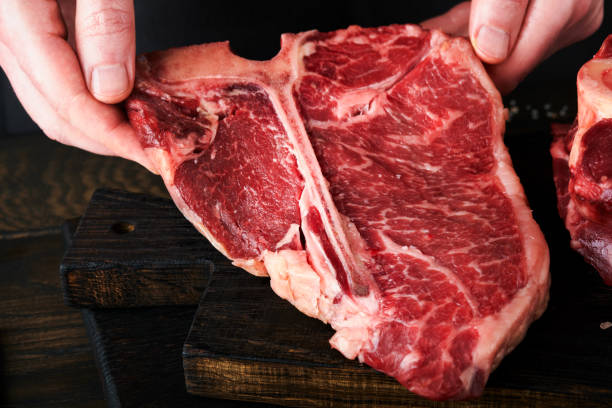 istock Chef cutting steak beef. Mans hands hold raw steak T-Bone on rustic wooden cutting board on black background. Cooking, recipes and eating concept. Selective focus. 1477500489