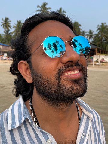 Stock photo showing an Indian man on holiday in Goa, South India, pictured standing wearing tinted, mirrored sunglasses on Palolem Beach, a particularly popular winter holiday destination for both English and German tourists.