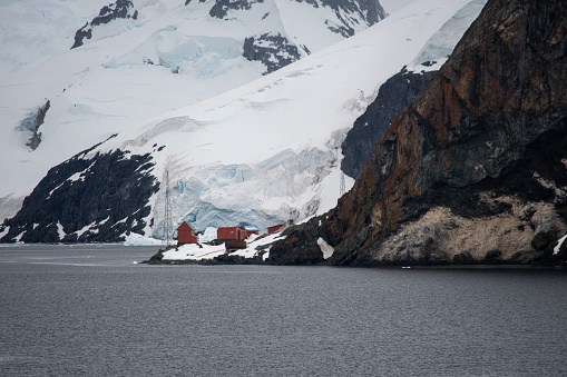 A wide shot of Base Brown (Argentina) in Antarctica set amongst cliffs, water and ice in a bleak landscape