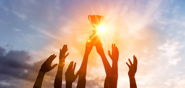 Silhouette Business team holding award trophy show victory business success sunset background. Winning team with trophy cup against shining sun in sky. Man holding trophy cup Success of teamwork, joint achievement of goal in business and life. Winning team is holding trophy in hands. Silhouettes of many hands in sunset. winning stock pictures, royalty-free photos & images