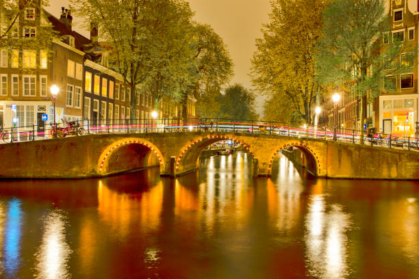 malowniczy nocny widok na pejzaż miejski amterdam z jednym kanałami wraz z oświetlonym mostem i tradycyjnymi holenderskimi domami o zmierzchu w tle - niderlandy zdjęcia i obrazy z banku zdjęć