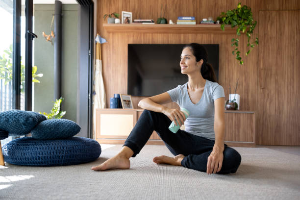 Happy Brazilian woman sitting on the floor drinking water after finishing her home workout