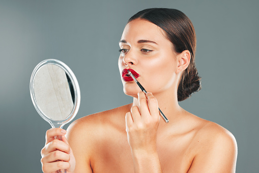 Lipstick, mirror and woman face getting ready with cosmetics and makeup brush. Mouth, female and beauty model looking at reflection with cosmetic tool with isolated studio background and lips product