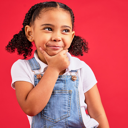 Little girl, face or thinking hand on chin on isolated red background in games innovation, studio question or fun vision. Smile, happy or curious child with ideas, fashion clothes or curly hair style