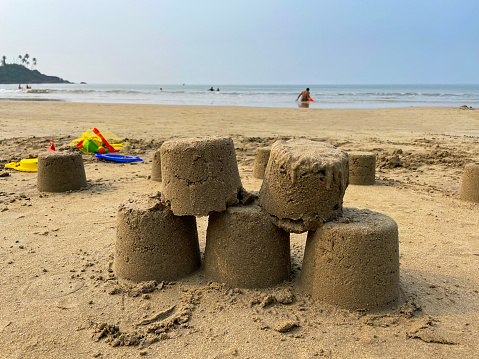 Stock photo showing close-up view of a group of sandcastles on a sandy beach, made by children during their summer holiday. These sand castles were made using typical plastic seaside buckets and spades, and are pictured with the blue sea in the background.
