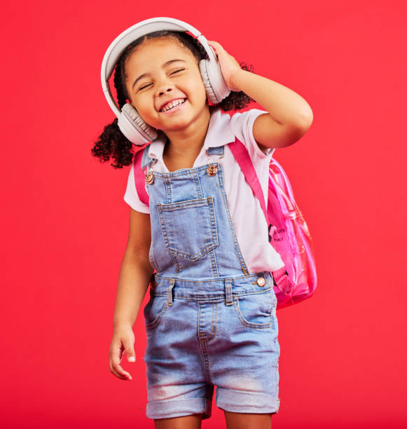 studente, bambino o cuffie per musica, podcast scolastici o radio educativa in canzoni, suoni o audio di apprendimento. sorridi, felice o bambino che ascolta i media di studio divertenti con lo zaino su sfondo rosso - one kid only audio foto e immagini stock