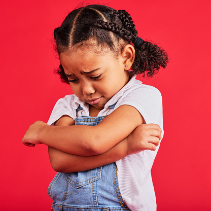 Kid, arms crossed or crying expression on isolated red background in depression, mental health or burnout. Upset, unhappy or little girl with sad, sulking or grumpy face in bullying crisis or anxiety