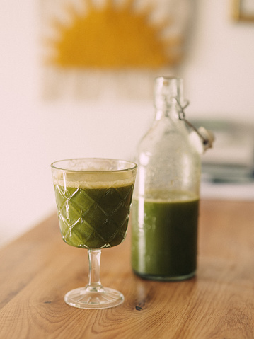 Green freshly pressed juice in glass and bottle 
Photo taken indoors in natural light