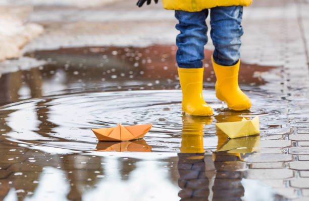 istock It's springtime. A small child in yellow rubber boots jumps through puddles, plays and launches paper boats on the water.. Photo of spring and autumn holidays. The concept of spring. 1477515516